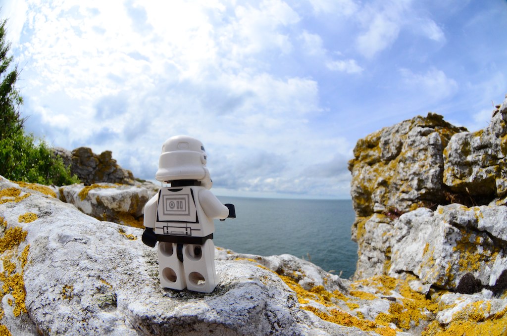 Lego Stormtrooper standing on a rock looking out over a sunny coastal scene