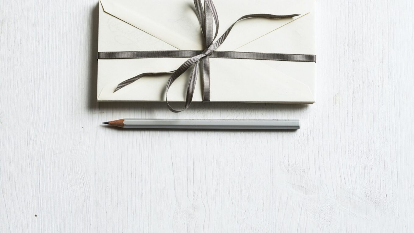 Envelopes, bound in a white ribbon, on a table with a pencil laid next to them