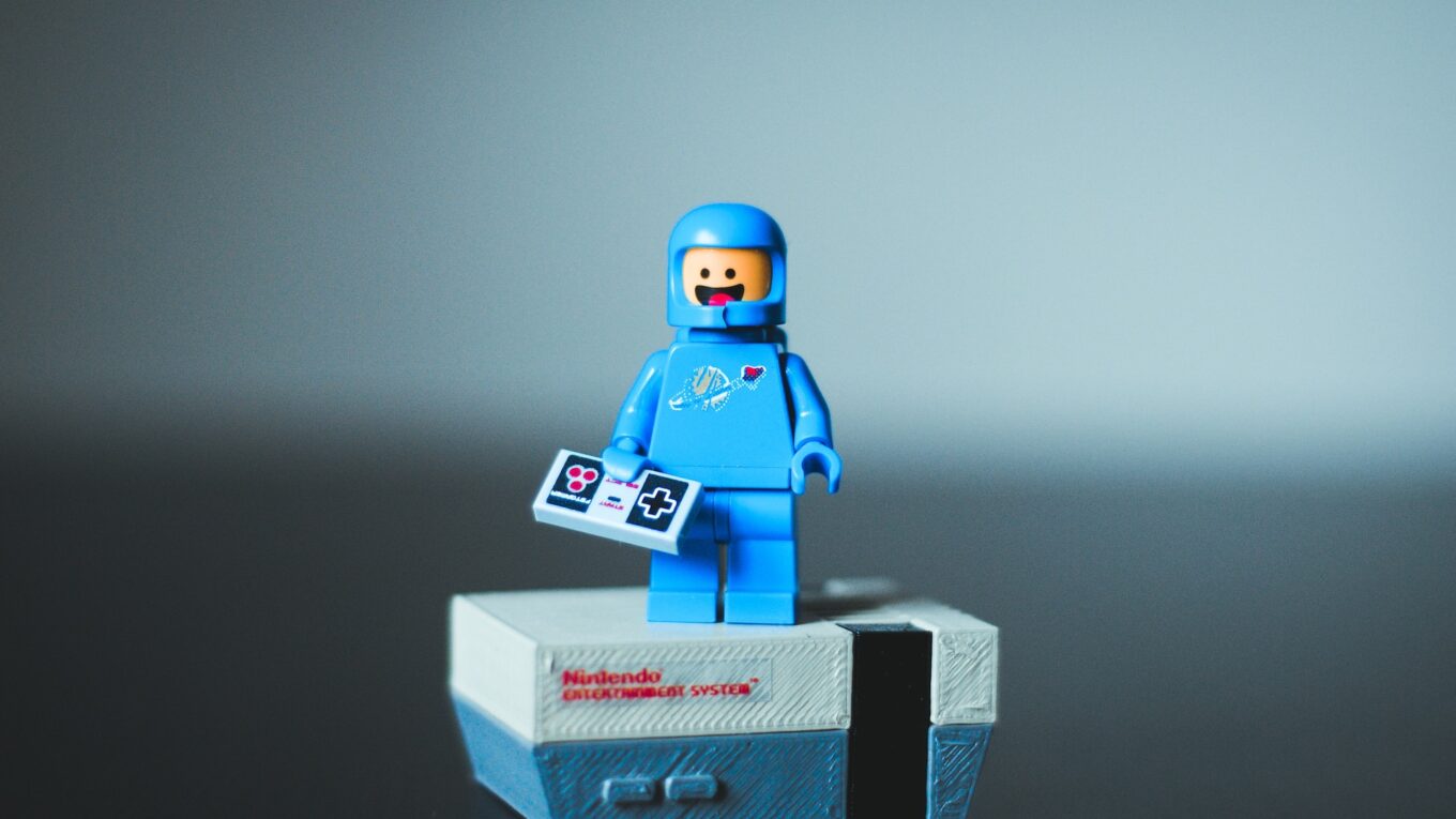 Blue Lego spaceman (Benny) standing on top of a 3D printed micro-Nintendo NES)